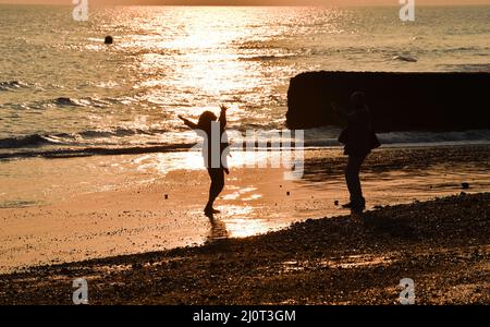 Brighton UK 20th March 2022 - A young woman dances on the sand at low tide as the sun sets on Brighton beach during the Spring Equinox as warm sunny weather is forecast to continue throughout Britain over the next week : Credit Simon Dack / Alamy Live News Stock Photo