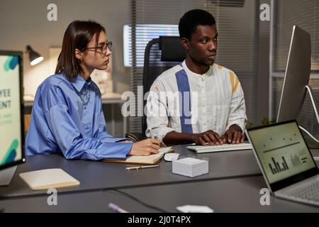 Portrait of young African American man using laptop while collaborating with female colleague in office Stock Photo