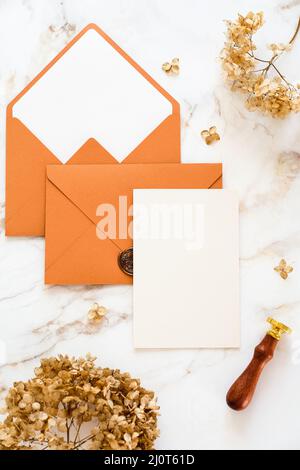 Wedding invitation card, brown envelopes, dry flowers on marble table. Flat lay, top view, copy space. Stock Photo