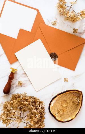 Bronze wedding envelopes, wedding invitation card mockup, wax seal stamp, golden ring, dry flowers on marble desk. Stock Photo