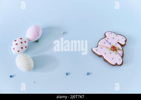 Close-up of three Easter eggs with a pattern of hearts and lines on a blue background and a gingerbread in the form of an Easter bunny. Top view with copy space. High quality photo Stock Photo