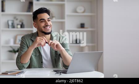 Dreamy Young Arab Man Sitting At Desk With Laptop In Home Office Stock Photo