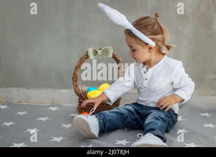 Cute Little Boy Dressed as a Bunny with Basket Full of Colorful Easter Eggs. Egg Hunting. Happy Christian Spring Holiday. Stock Photo