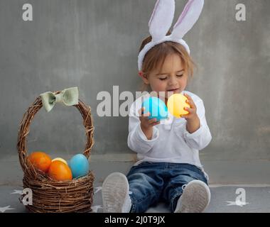 Portrait of Cute Little Baby Boy with Nice Rabbit Ears. Basket Full of Colorful Eggs. Happy Easter Celebration. Stock Photo