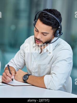 Let me walk you through it.... Shot of a young businessman making notes while working in a call center. Stock Photo