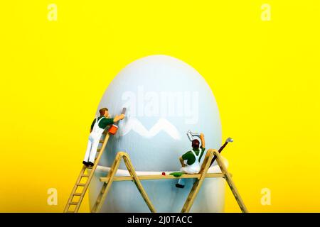 Conceptual image of miniature figure people painting a hens egg for Easter Stock Photo