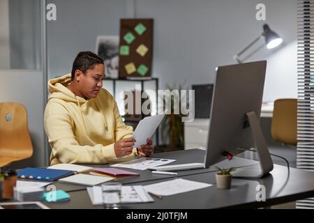Side view portrait of female designer working late in office and looking at documents Stock Photo