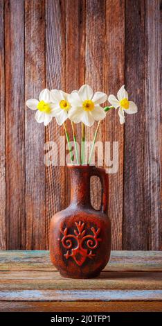 Still life of a bouquet of daffodils flowers in an old ceramic jug on a wooden vintage grunge background closeup Stock Photo