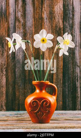 Still life of a bouquet of daffodils flowers in an old ceramic jug on a wooden vintage grunge background closeup Stock Photo