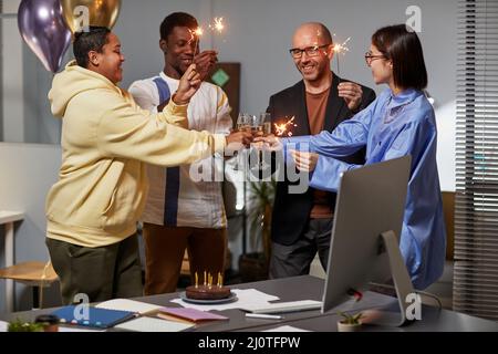 Diverse group of colleague lighting sparklers while celebrating Birthday in office Stock Photo