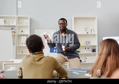 Front view portrait of African American science teacher explaining chemistry to group of children in school class and holding molecule models Stock Photo