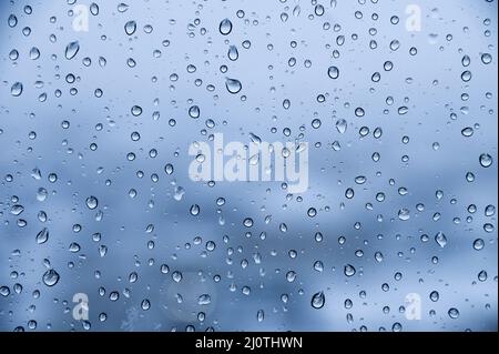 Water droplets on glass in rainy weather with small town sleeping areas out of focus in the background. Autumn cold wet backgrou Stock Photo