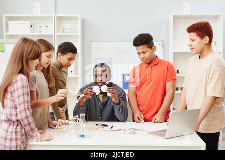 Front view at diverse group of children standing by African American teacher in chemistry class at school Stock Photo