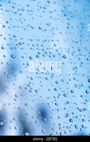 Vertical shot. Shallow depth of field Water droplets on glass in rainy weather with small town sleeping areas out of focus in th Stock Photo