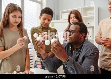 Side view portrait of African American teacher explaining molecule structure to diverse group of children in chemistry class Stock Photo