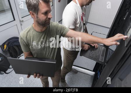 Technicians team updating hardware inspecting system performance in super computer server room or cryptocurrency mining farm. Stock Photo