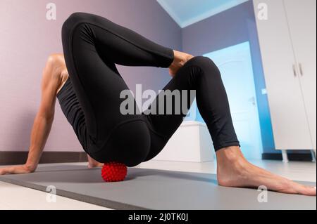 Close-up young caucasian woman doing myofascial self-massage of her thigh and buttocks with a massage ball on a massage mat. 4k Stock Photo