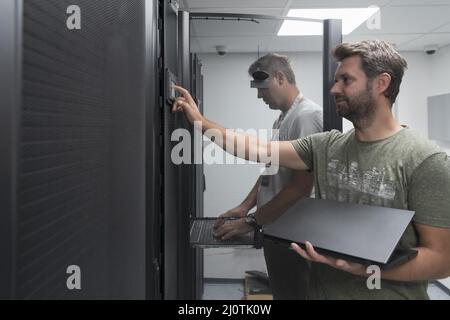 Technicians team updating hardware inspecting system performance in super computer server room or cryptocurrency mining farm. Stock Photo