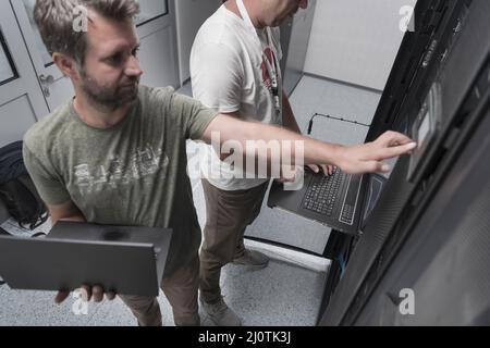 Technicians team updating hardware inspecting system performance in super computer server room or cryptocurrency mining farm. Stock Photo