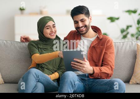 Happy Middle Eastern Spouses Using Digital Tablet Sitting At Home Stock Photo