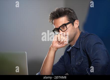 Bringing his business into focus. A thoughtful young entrepreneur using his laptop. Stock Photo
