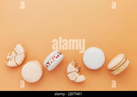 White, yellow, gold macaron cookies. Colorful, sweet small French macaroon cakes laying on the table. Light yellow-beige background. Broken cut, bitten parts, halves. High quality photo Stock Photo