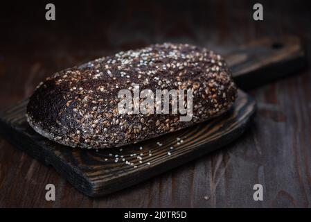 Whole rye bread covered with hemp seeds on the old wooden board Stock Photo