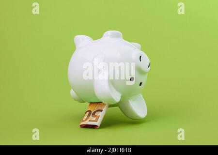 Piggy bank with fifty Euro fall on the green background Stock Photo