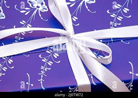 Gift box packaged inside blue decorative paper and tied with white bow Stock Photo