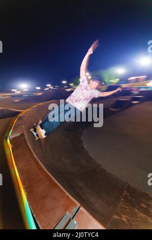A young skateboarder rides at speed sideways along the ramp by spreading his hands to the sides. Night shot with long exposure a Stock Photo