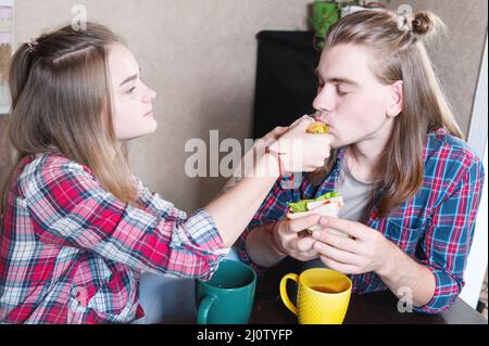A young attractive couple has breakfast in their home kitchen. They feed each other and laugh. The concept of healthy eating in Stock Photo