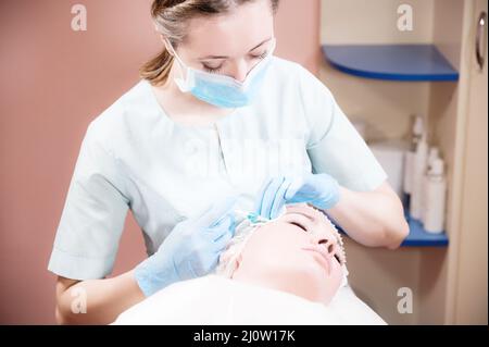 A female beautician makes an injection to a female client in a cosmetics office. Cosmetic procedures for rejuvenation Stock Photo