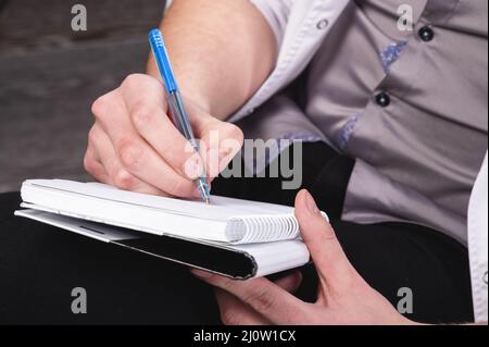 The men's hands of a psychologist doctor in a white robe hold a notebook and a ballpoint pen with a notebook ready to record the Stock Photo