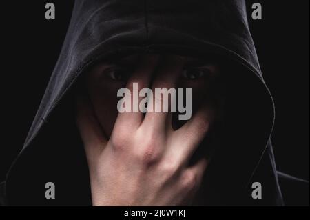 A low key portrait of a man in a hooded hand gesture makes a sperm hero mask. The concept of anonymity and privacy Stock Photo