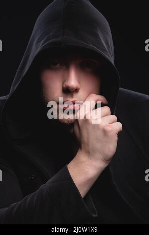A low key portrait of a man in a hooded hand gesture makes a sperm hero mask. The concept of anonymity and privacy Stock Photo