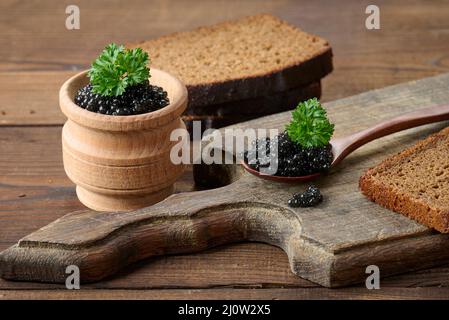 Fresh grainy black paddlefish caviar in brown wooden spoon on a brown table, close up Stock Photo