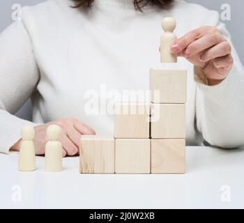 Woman in a white sweater puts a wooden figurine on the podium. The concept of employee search, career advancement. Talented empl Stock Photo