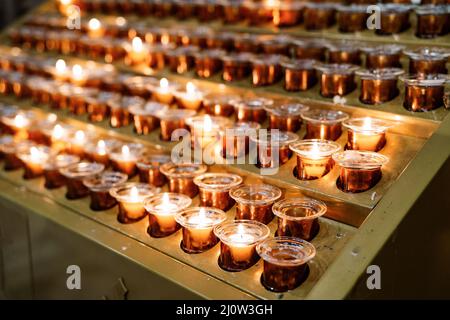Votive candles burn in rows on a stand in the temple. Close-up Stock Photo