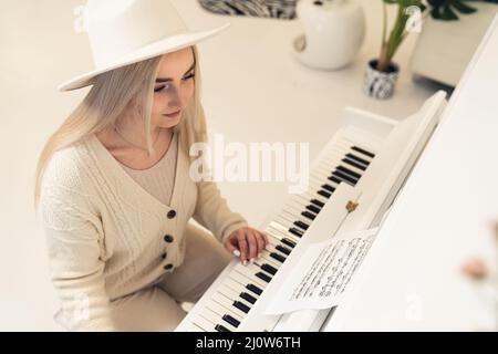 Young blond Caucasian woman in light clothes playing the piano copy space . High quality photo Stock Photo