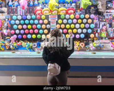 Back of a woman standing while throwing a dart at a night-time fair Stock Photo
