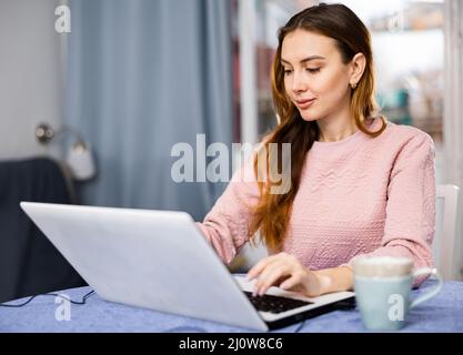 Portrait of young woman sitting at table in living room looking laptop screen Stock Photo