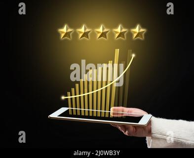 Female hand holds a tablet and five gold stars above it. App evaluation. User reviews, business rating Stock Photo