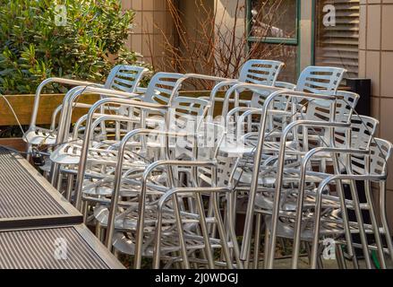 Close-up on a pile of aluminum chairs. Pile of chairs at the backyard of a street cafe. Street photo, selective focus, nobody Stock Photo