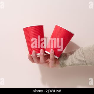hand holds paper cardboard red cup for coffee, yellow background. Eco ...