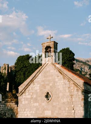 Old small chapel with a bell on the roof surrounded by trees Stock Photo