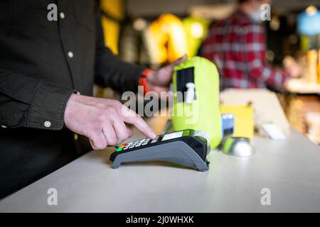 Close-up of the hands of a male salesman cashier holding POS terminal and paper receipt behind the counter of a sports store. Ca Stock Photo