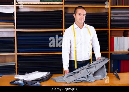 Portrait of concentrated young handsome tailor working in mens cloths store Stock Photo