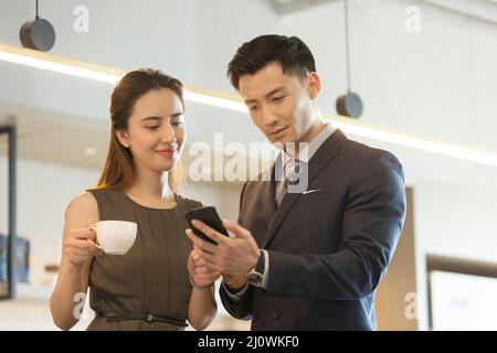 Smiling elegant Chinese business colleagues enjoying coffee and exchanging contacts in office Stock Photo
