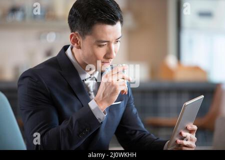 Successful Chinese businessman looks at a digital tablet over a drink Stock Photo