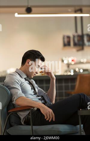 Tired Chinese young business man drinking alcohol and relaxing in the hotel bar Stock Photo